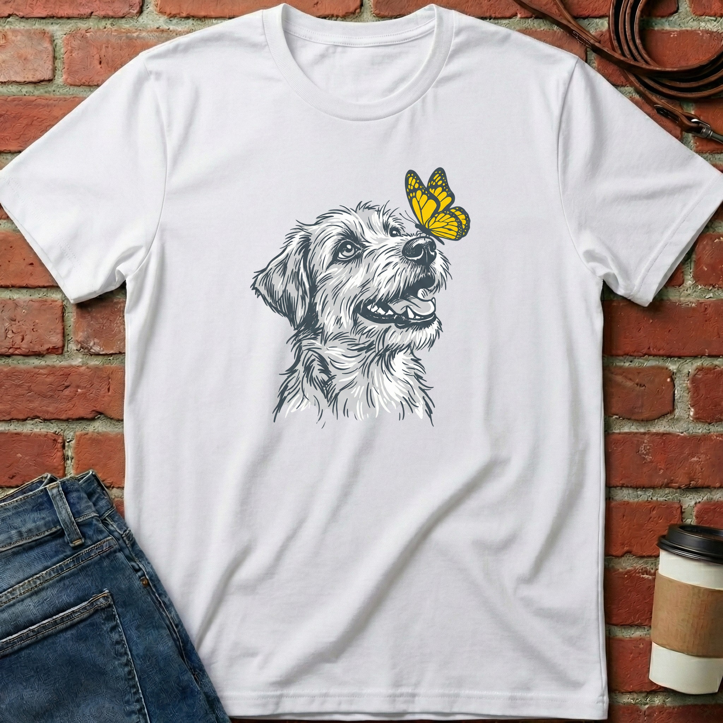 White t-shirt with a dog and butterfly graphic on a brick wall background. Minimalist dog apparel by pemuyo.
