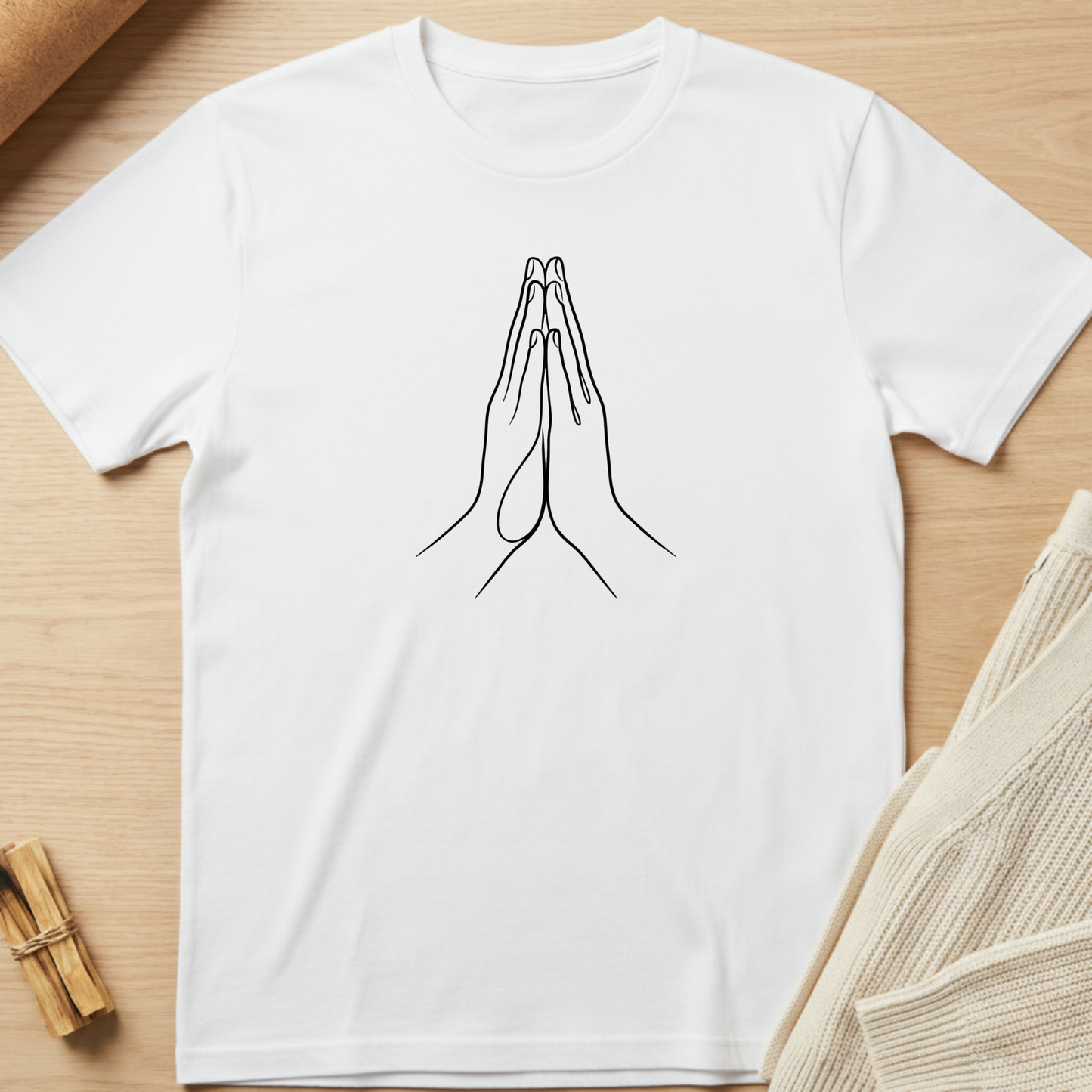 White t-shirt with a line drawing of praying hands on a wooden surface. Minimalist yoga apparel by pemuyo.